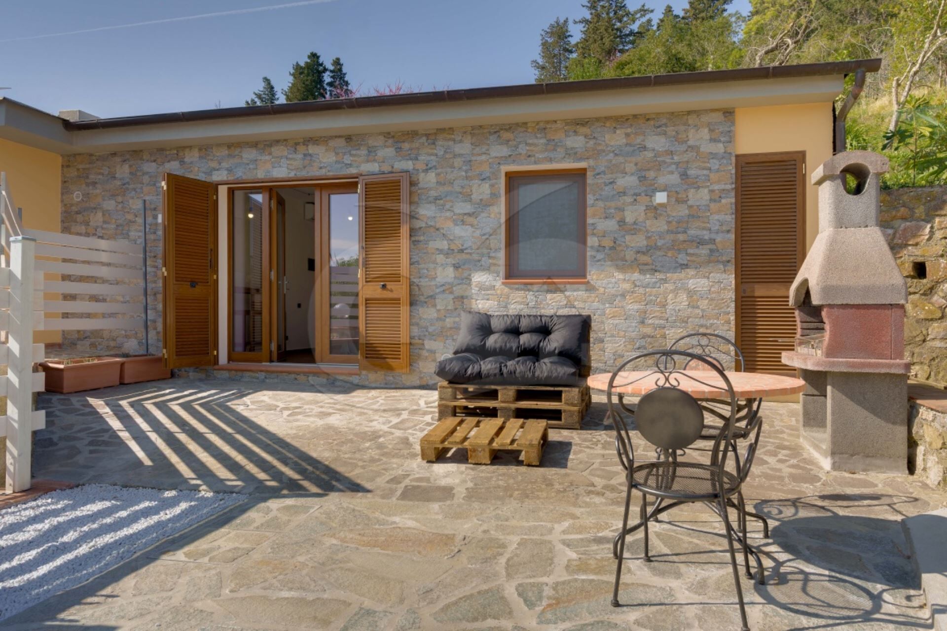 Un bâtiment en pierre doté d’un patio comprenant un banc en bois, une table avec des chaises et une cheminée en pierre.