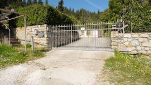 Ein begrenzter Eingang mit einer Steinmauer und einem Metallgitter, umgeben von Grünpflanzen und blauem Himmel.