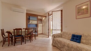 Una sala de estar con sofá, una mesa de comedor con sillas, una zona de cocina y una puerta que da al exterior.