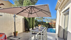 An outdoor patio with a table set for dining, a large umbrella, and a swimming pool in the background. - Beautiful villa, sea view, swimming pool, WIFI (ST MANDRIER SUR MER)