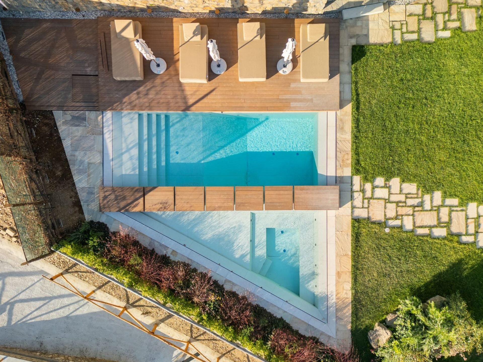 Vista aérea de uma piscina moderna ao ar livre, com espreguiçadeiras de madeira e caminho de pedra.