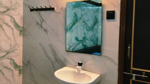 A bathroom with a marble wall, a sink, a mirror, and a door. - Guru Mauli Yatri Nivas (Shirol)