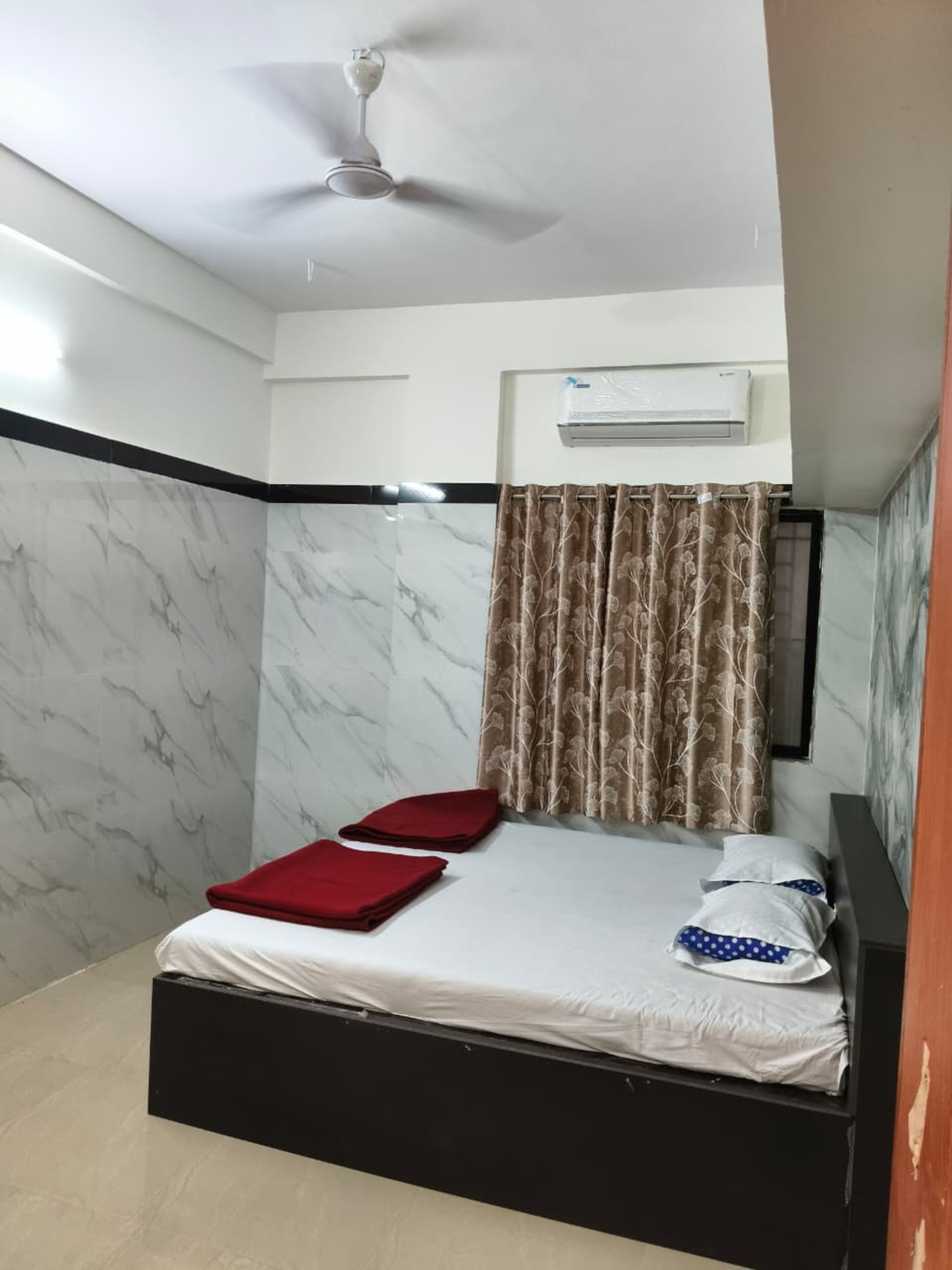 A bedroom with a bed, a ceiling fan, an air conditioning unit, and a window with curtains.
