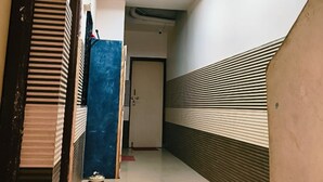 A narrow hallway with a welcome mat, a blue door, and a ceiling light fixture. - Guru Mauli Yatri Nivas (Shirol)