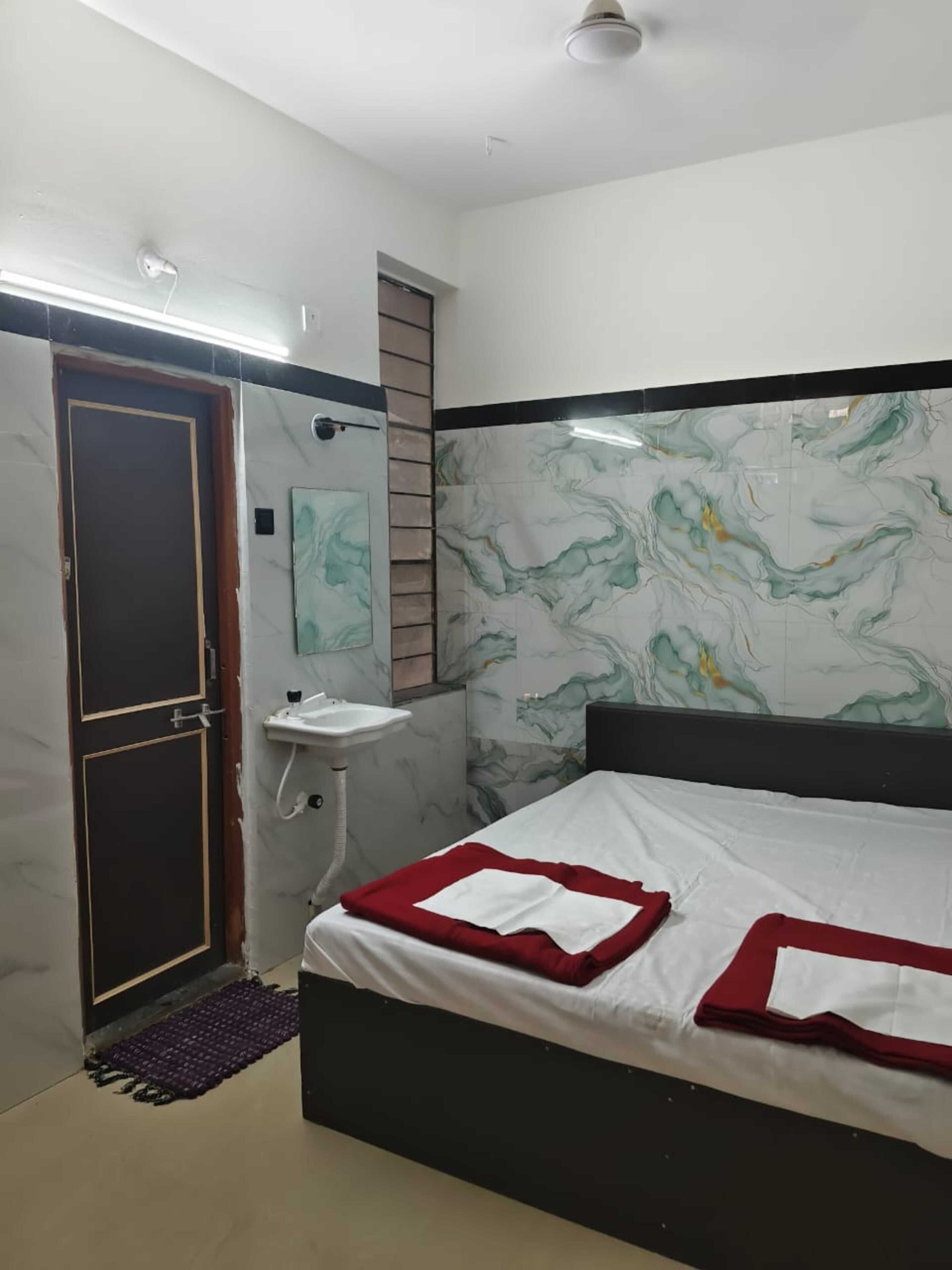 A bedroom with a bed, a bedside table, a wall-mounted sink, and a door.
