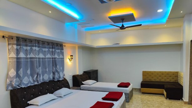 A hotel room with two beds, a ceiling fan, a sofa, and a red rug. - Guru Mauli Yatri Nivas (Shirol)