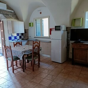 Eine Küche mit Esstisch, Stühlen, einer Mikrowelle, einem Kühlschrank und einem Fernseher.