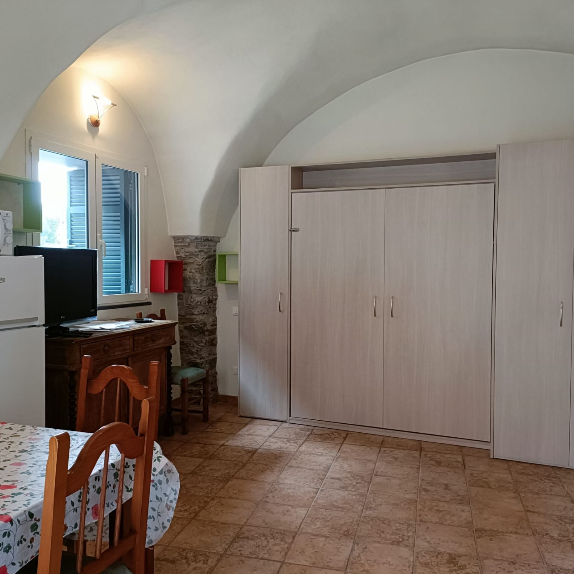 Une cuisine équipée d’une table à manger, de chaises, d’un téléviseur, de placards et d’un mur en pierre.