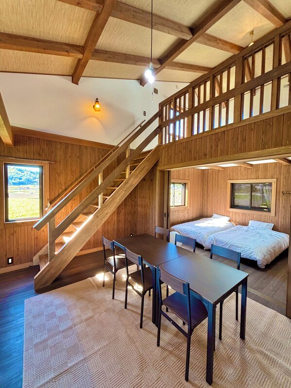 A wooden interior with a staircase, a dining table with chairs, and two beds.