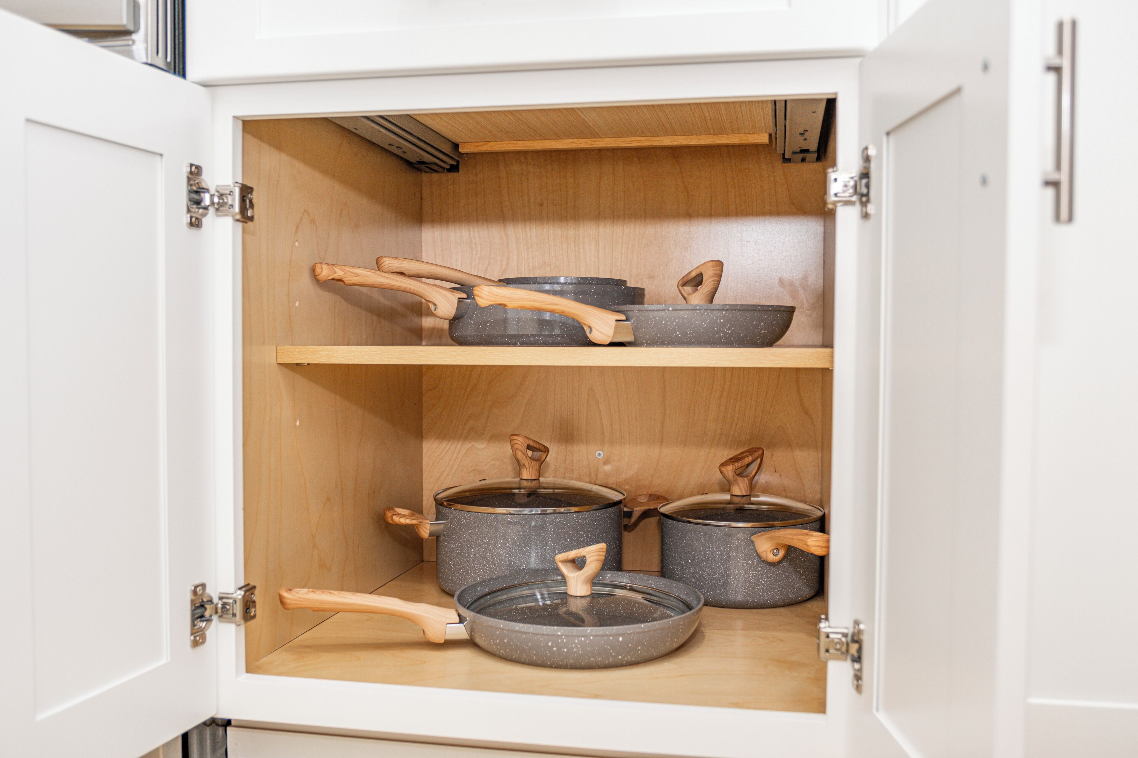 A kitchen cabinet with two shelves, each holding pots with wooden handles.