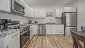 A modern kitchen with white cabinets, stainless steel appliances, a granite countertop, and a wooden floor. - Cozy Carnegie Retreat • Minutes to Downtown PGH (Carnegie)