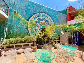 An outdoor seating area with metal chairs and tables, surrounded by potted plants and a decorative wall mural. - Whost Hostel (Mexico City)