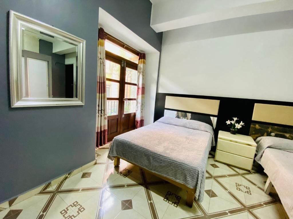 A bedroom with a bed, bedside tables, a mirror, and a window with curtains.