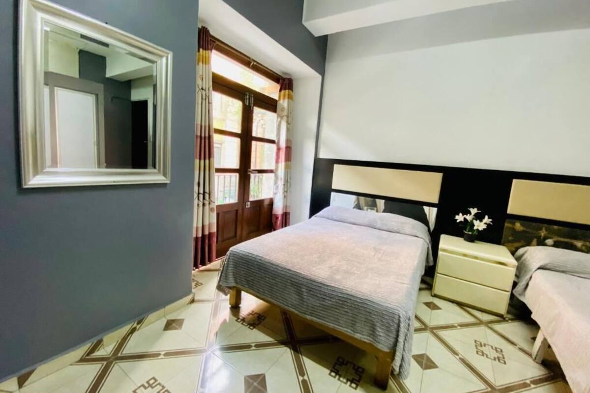 A bedroom with a bed, bedside tables, a mirror, and a window with curtains.
