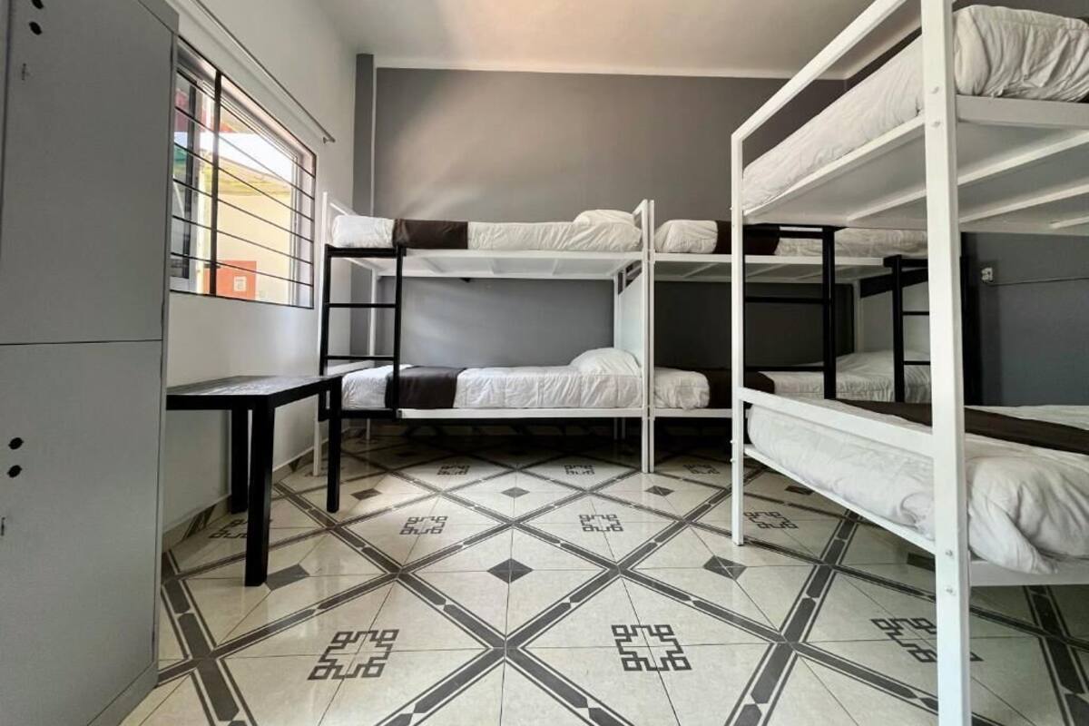 A dormitory room with bunk beds, a window with bars, and a tiled floor.