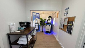 A hotel lobby with a reception desk, a self-service kiosk, a plant, and a bulletin board. - Sunshine Inn (Holiday)