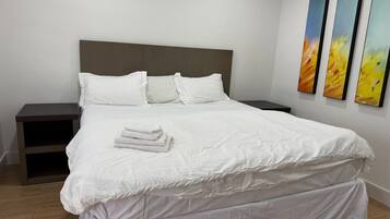 A neatly made bed with white linens, a wooden headboard, and a nightstand with a drawer.