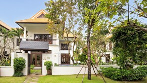 Uma casa de dois andares com varanda, um pequeno jardim e uma árvore no quintal.