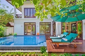 A swimming pool with lounge chairs and an umbrella, surrounded by a wooden deck and greenery. - Koaniva Luxury Villa Beach Da Nang (Da Nang)