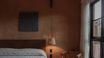 A bedroom with a bed, a chair, a table, a lamp, and a large window.