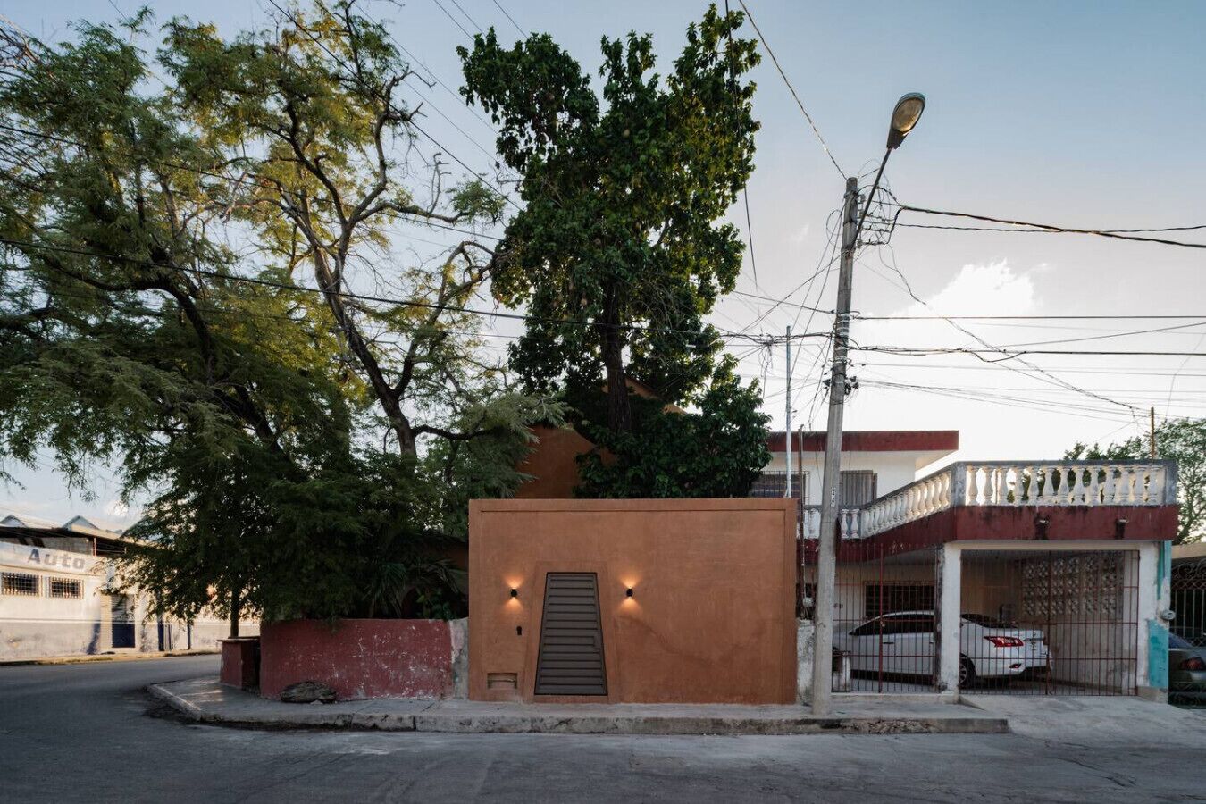 A small building with a door and two lights, surrounded by trees and a street.