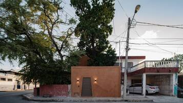 A small building with a door and two lights, surrounded by trees and a street.