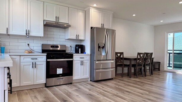 A modern kitchen with white cabinets, stainless steel appliances, and a dining area with wooden chairs. - USC Private Suite & Bath/Long-Term/Utilities, Wi-Fi & Laundry Incl. 4m to campus (Los Angeles)