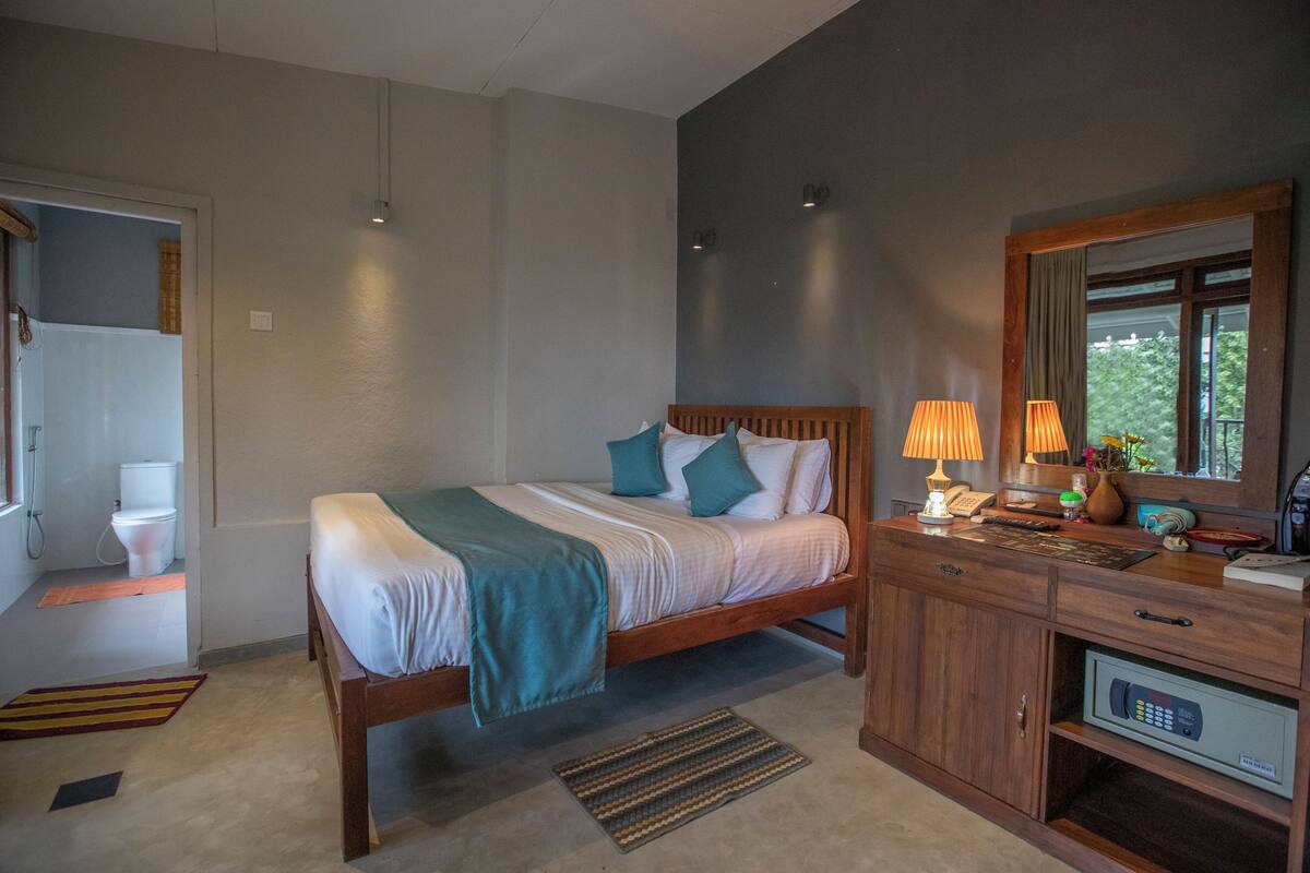 Un dormitorio con cama, mesita de noche, lámpara y vistas al exterior.