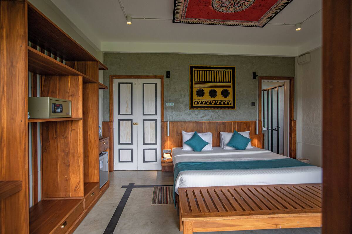 Habitación de hotel con cama, muebles de madera, una obra de arte colgada en la pared y una puerta con diseño geométrico.