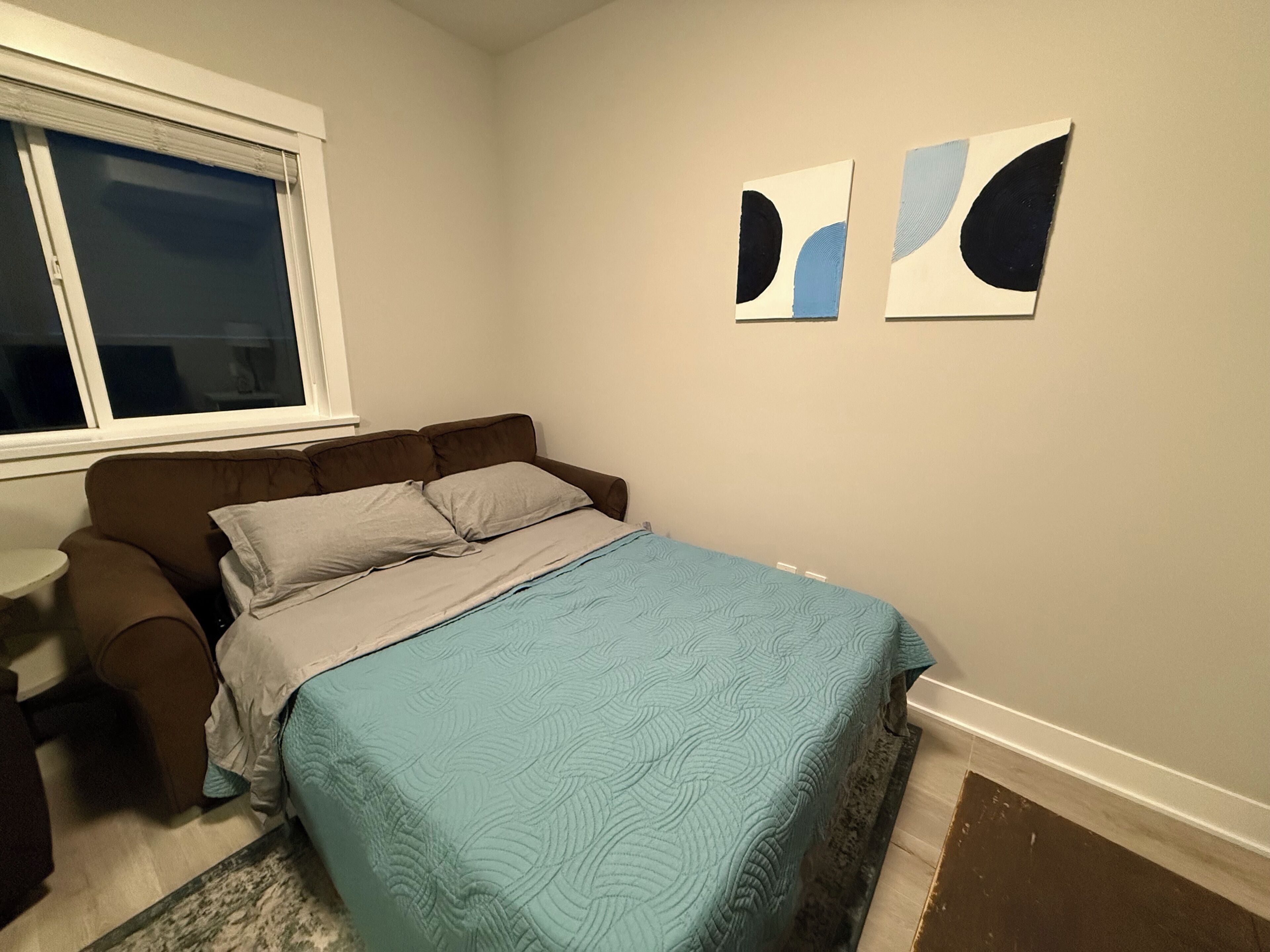A bedroom with a bed, a window, and two wall art pieces.