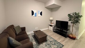 Una sala de estar con un sofá marrón, una mesa de centro, un televisor, una planta y arte abstracto en la pared.