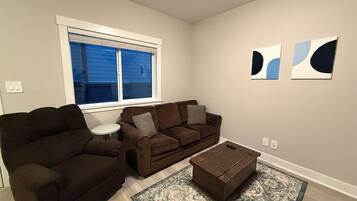 A living room with a brown sofa, a small white table, a coffee table, and abstract wall art.
