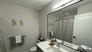 Un baño moderno con un lavamanos blanco, un espejo grande y un inodoro.