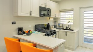 A kitchen with white cabinets, a black microwave, a stove, and a sink. - Blue Haven Suite at Black Pineapple Cottages (Cedar Grove)