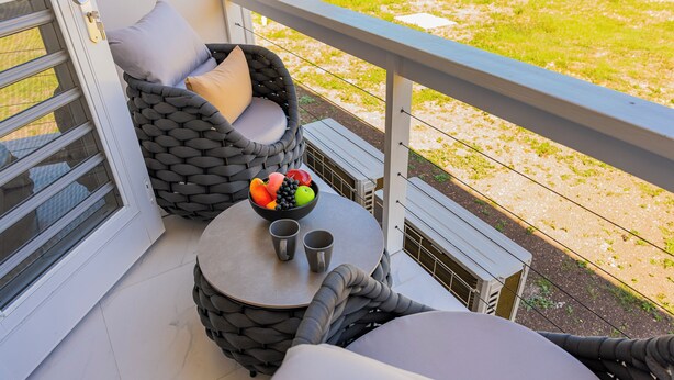 A balcony with a wicker chair, a small table with a bowl of fruit and two cups, and a white railing. - Blue Haven Suite at Black Pineapple Cottages (Cedar Grove)