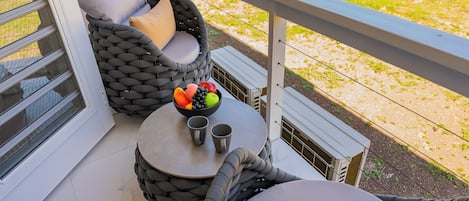 Ein Balkon mit Korbstuhl, einem kleinen Tisch mit einer Obstschale und zwei Tassen, sowie einem weißen Geländer.