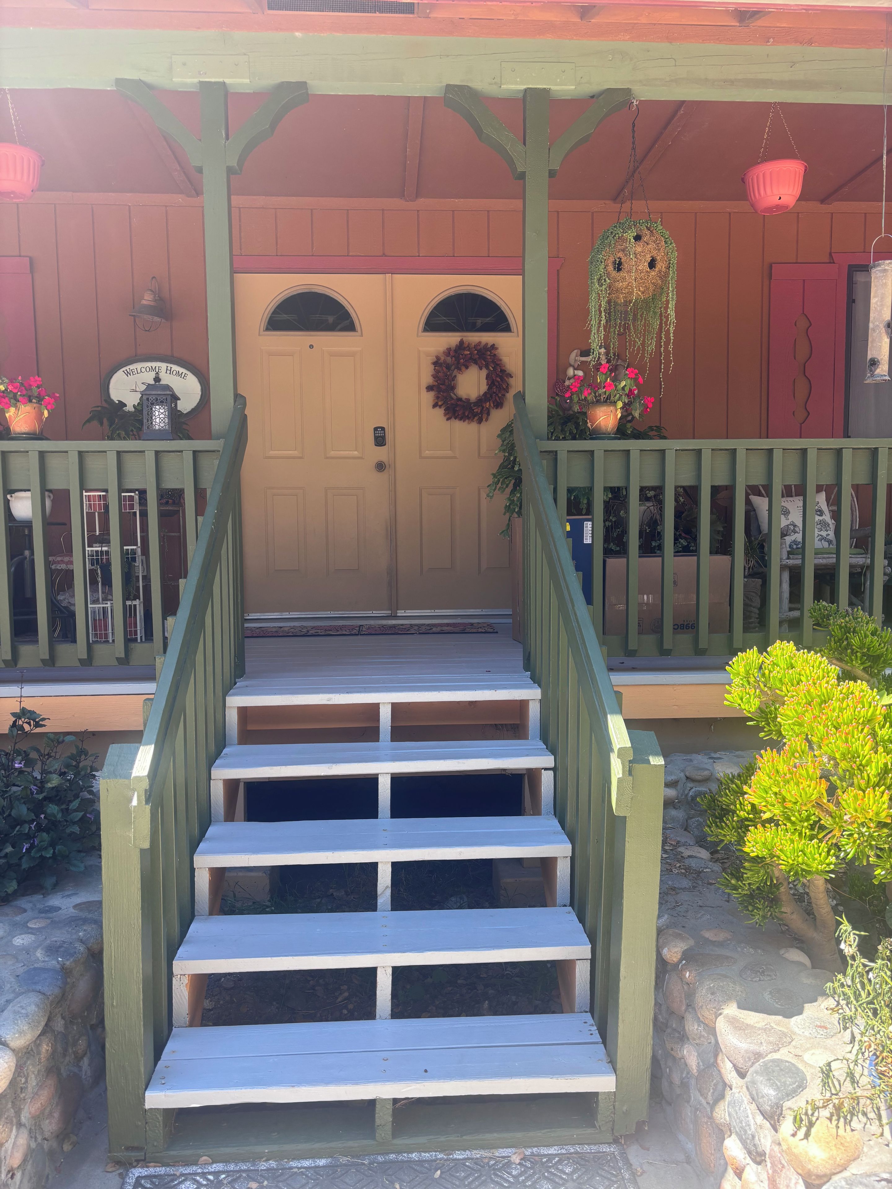 A wooden staircase leading to a door with a wreath and a welcome sign.