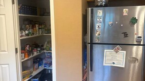 A kitchen with a stainless steel refrigerator, wooden cabinets, and a pantry filled with food items.
