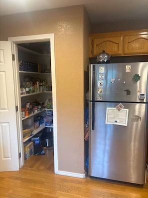 A kitchen with a stainless steel refrigerator, wooden cabinets, and a pantry filled with food items. - Pine Canyon retreat (Salinas)