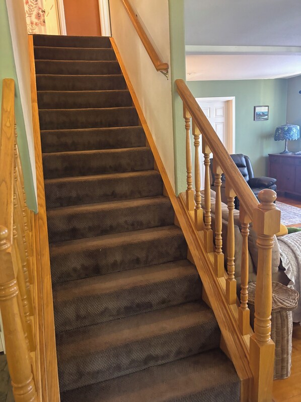 A carpeted staircase with wooden balusters, a door at the top, and a room with a chair and lamp. - Pine Canyon retreat (Salinas)