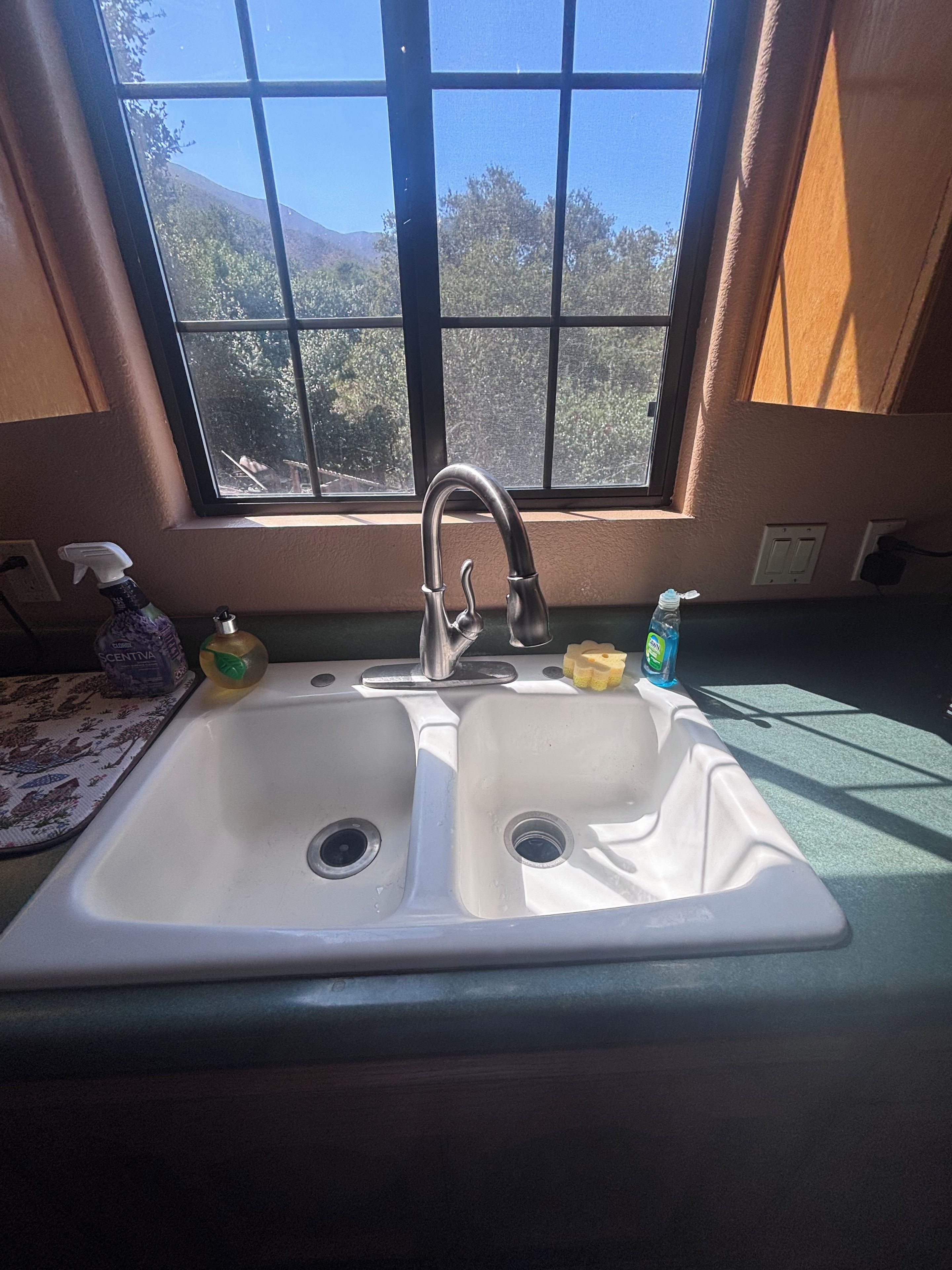 Une cuisine équipée d’un évier à deux bacs, d’une fenêtre et offrant une vue sur les arbres et les montagnes.