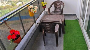 A balcony with a table and chairs, potted plants, and a view of buildings and greenery. - Cozy 1-BHK entire apartment at good height Balcony (Gurugram)