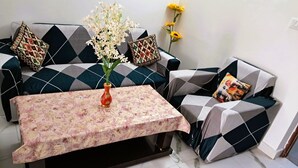 A living room with a sofa set, a coffee table, and a vase with flowers. - Cozy 1-BHK entire apartment at good height Balcony (Gurugram)