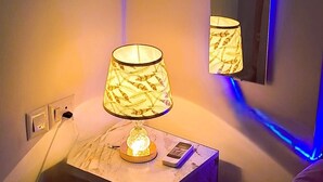 A bedside table with a lamp, a remote control, and a drawer. - Cozy 1-BHK entire apartment at good height Balcony (Gurugram)