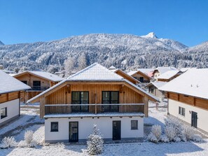 Um chalé de madeira com varanda, rodeado por árvores e montanhas cobertas de neve.
