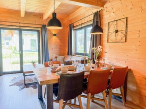 Un intérieur en bois avec une table à manger dressée pour quatre personnes, des fauteuils en cuir, une horloge au mur et de grandes fenêtres.