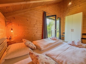 Une chambre dans un chalet en bois, avec deux lits, une table de chevet, une armoire et une vue sur l’extérieur grâce à une grande fenêtre.