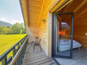 A wooden balcony with a glass door leading to a bedroom with a bed and a nightstand. - Lovely holiday home on park near ski resort (Rattendorf)