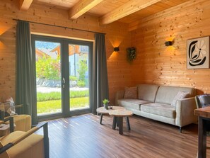 A cozy room with a wooden ceiling, a sofa, a coffee table, and a view through large sliding glass doors. - Lovely holiday home on park near ski resort (Rattendorf)