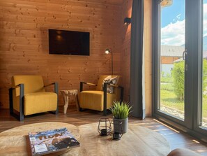A wooden interior with two yellow armchairs, a flat-screen TV, a floor lamp, a coffee table, and a potted plant. - Lovely holiday home on park near ski resort (Rattendorf)